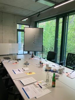 Besprechungsraum mit Tisch, Stühlen, Flipchart und Fenstern mit Blick ins Grüne.